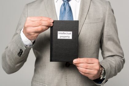 partial view of businessman holding juridical book with intellectual property title isolated on grey