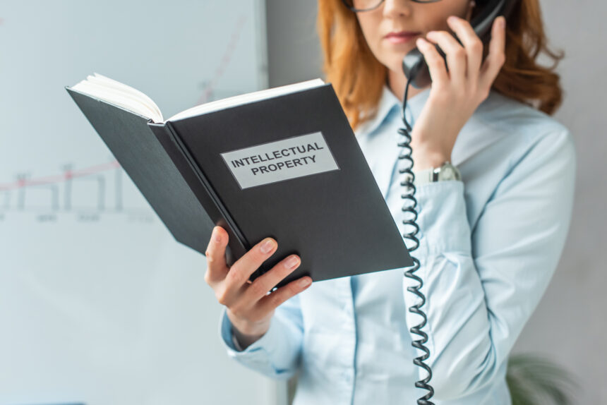 Cropped view of businesswoman holding book with intellectual property lettering, while talking on