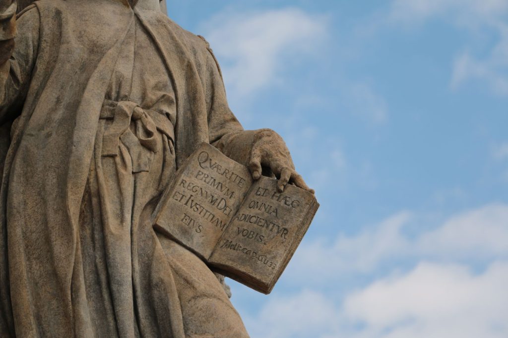 Montesquieu Separation of Powers Theory 2026 (Close-up of a historical stone statue holding an open book against blue sky.)