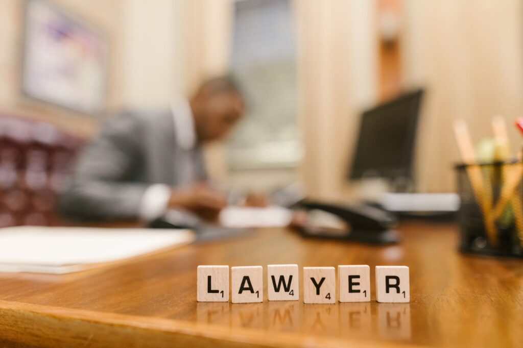 Wooden letter tiles spelling 'LAWYER' on a desk, with blurred office setting in the background.
