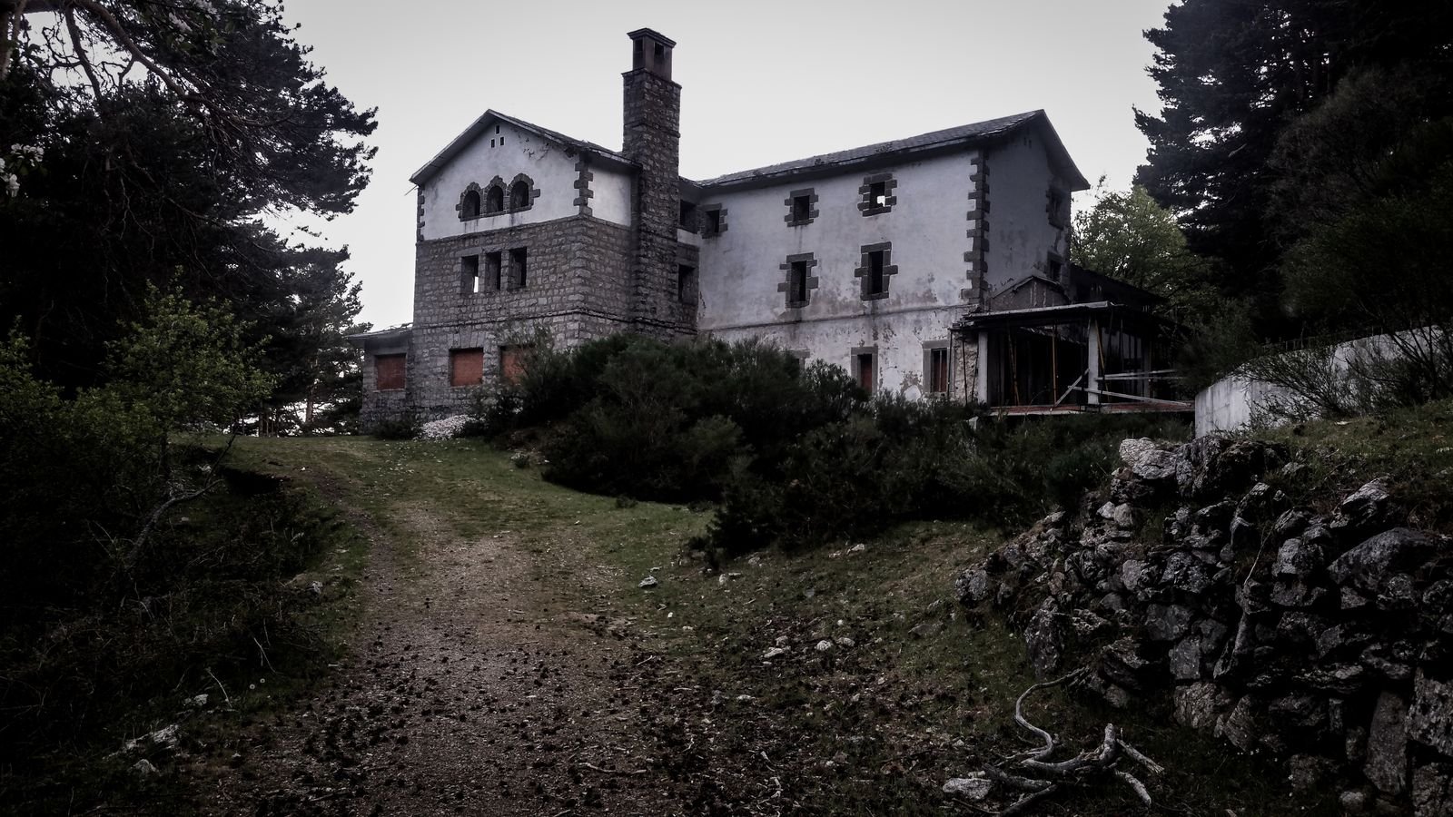 Abandoned stone house on a wooded hillside with an overgrown dirt path leading to it