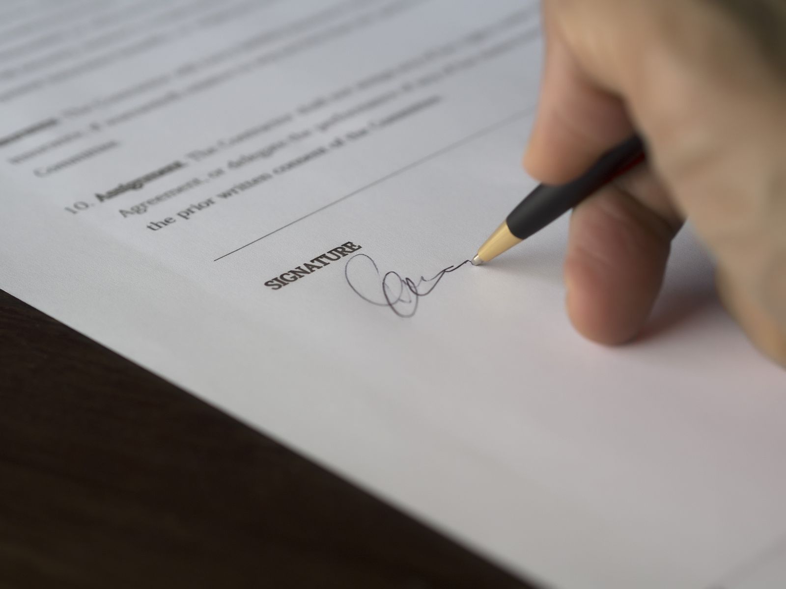 Close-up of a hand signing a printed contract on the signature line with a black and gold pen