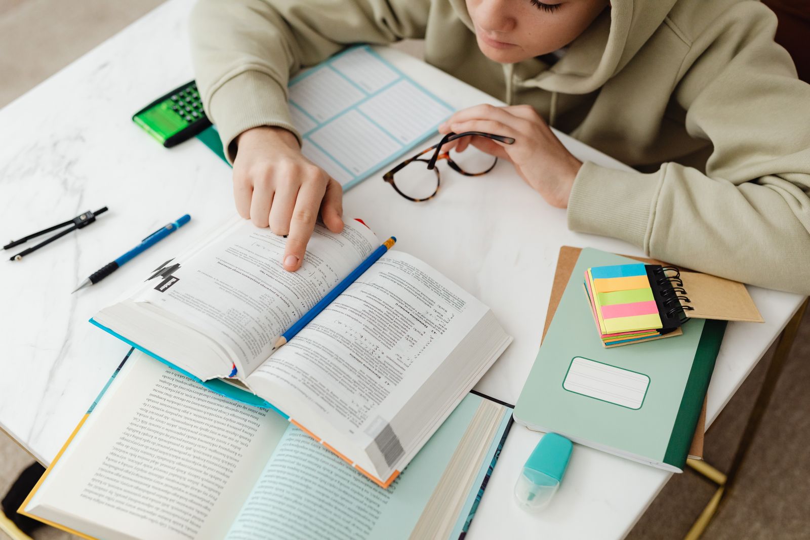 Student studying at a desk with open textbooks, glasses, a calculator and sticky notes