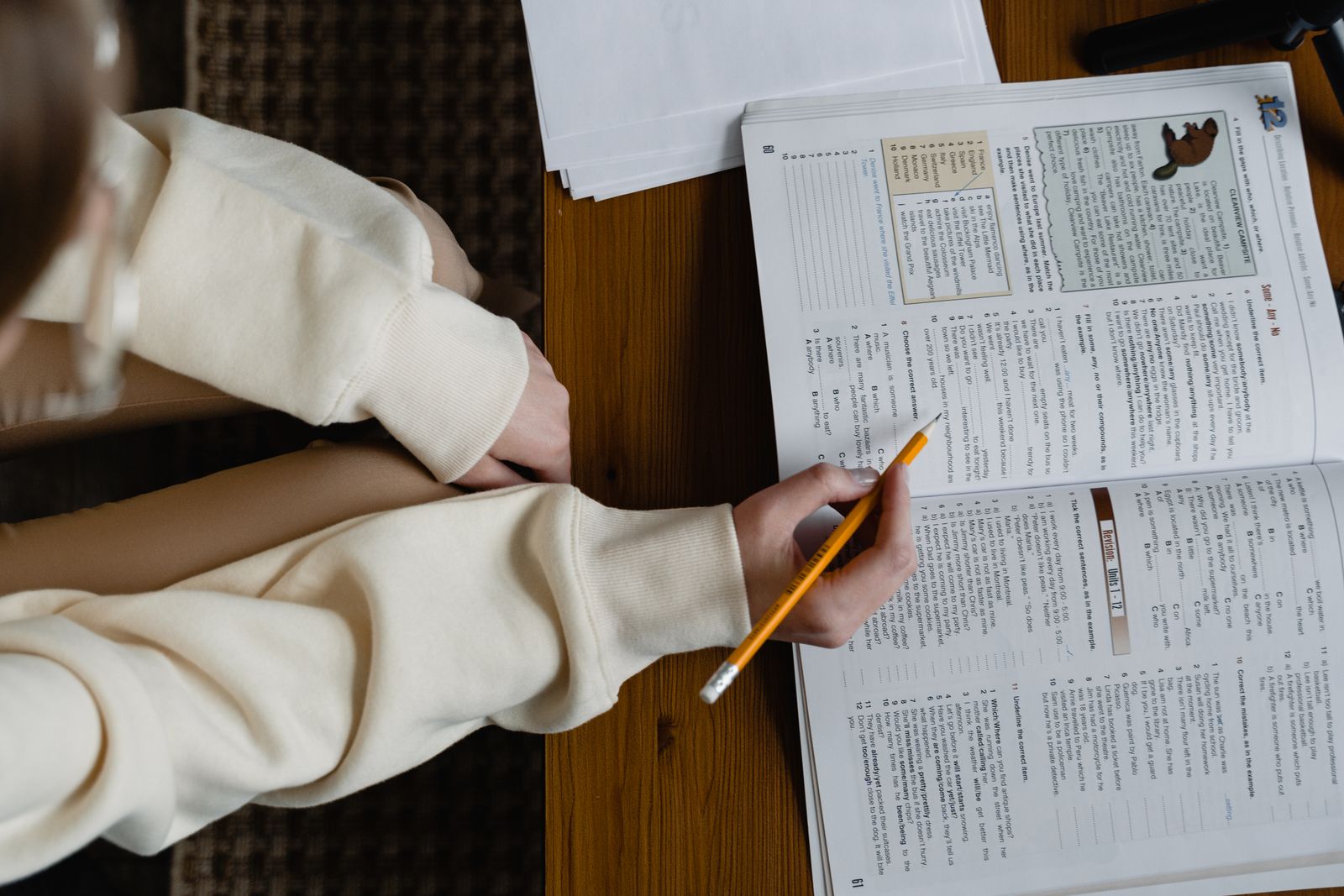 Student holding a pencil over an open study book filled with practice questions