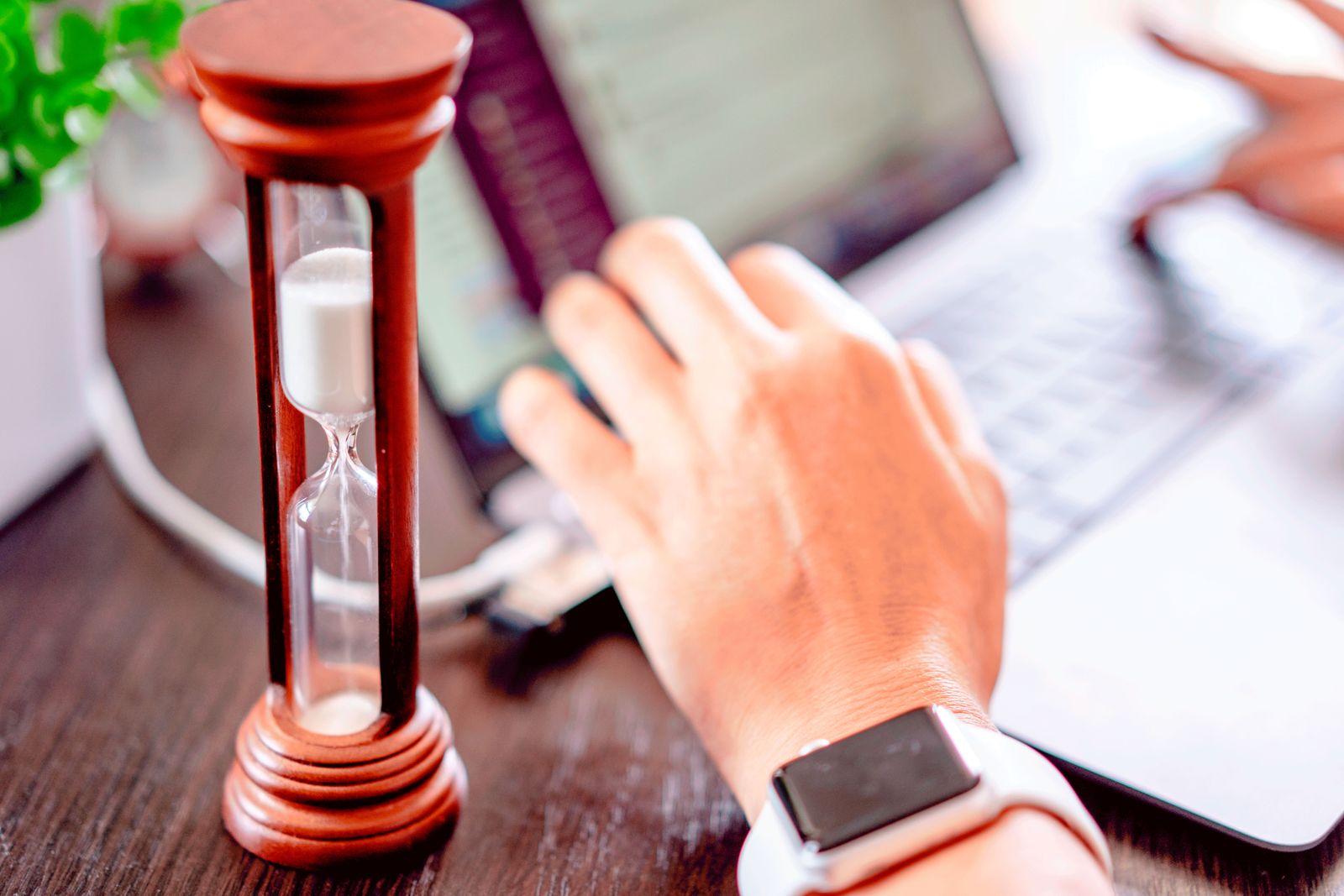 Red wooden hourglass beside a hand typing on a laptop, a reminder of time recorded in billable units