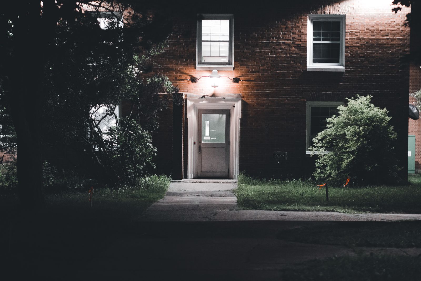 Brick house at night with a single lamp lighting the front door and the path leading up to it