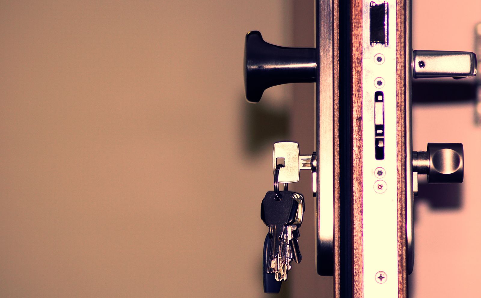 Close-up of the edge of an open front door showing the lock, handle and a bunch of keys in the keyhole