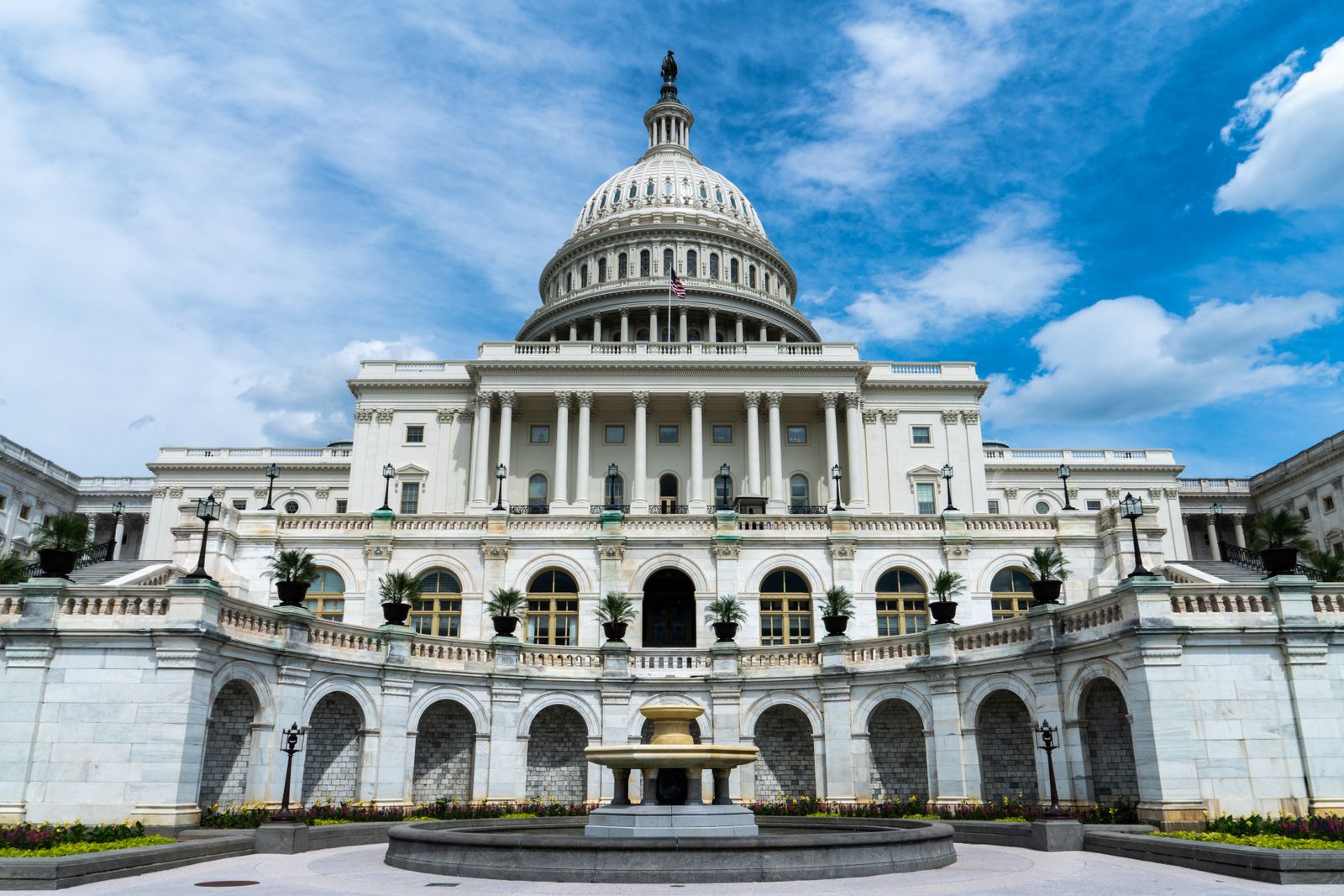 The US Capitol building in Washington with its dome and fountain under a blue sky with white clouds