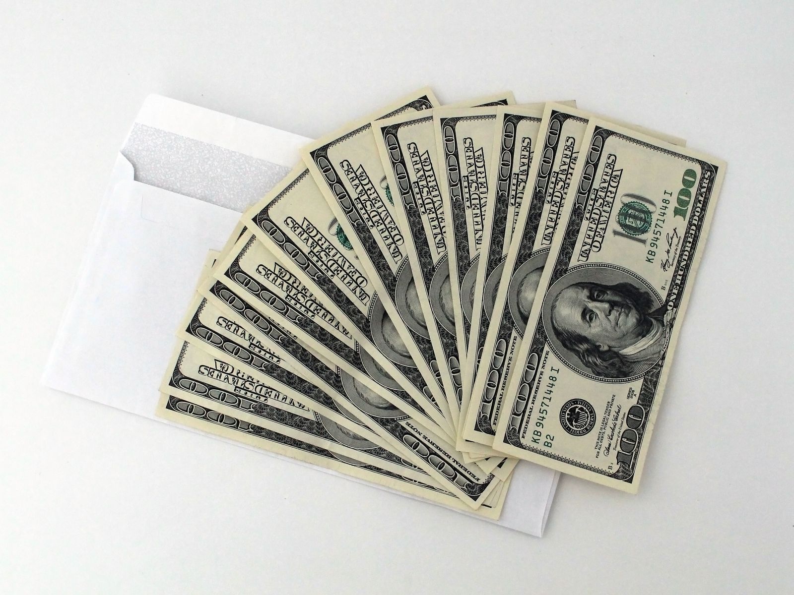 Fan of US 100 dollar bills spilling out of a white envelope on a white surface, a symbol of bribery