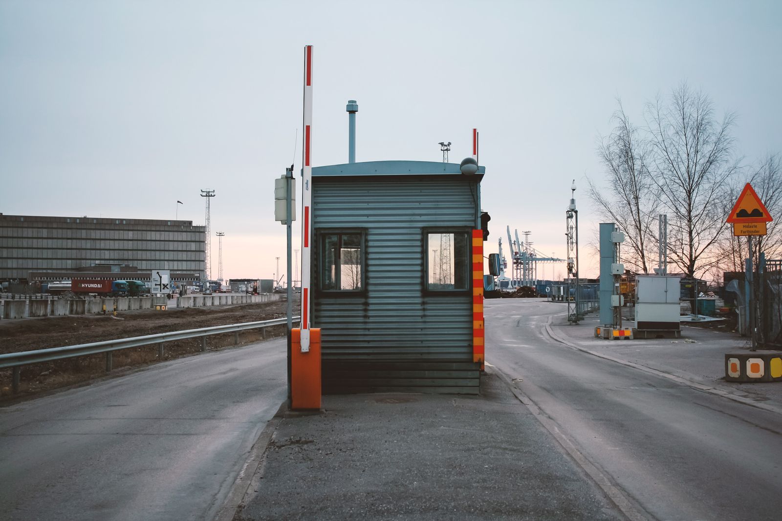Guard booth and raised barrier at the entrance to a port, with container cranes in the distance