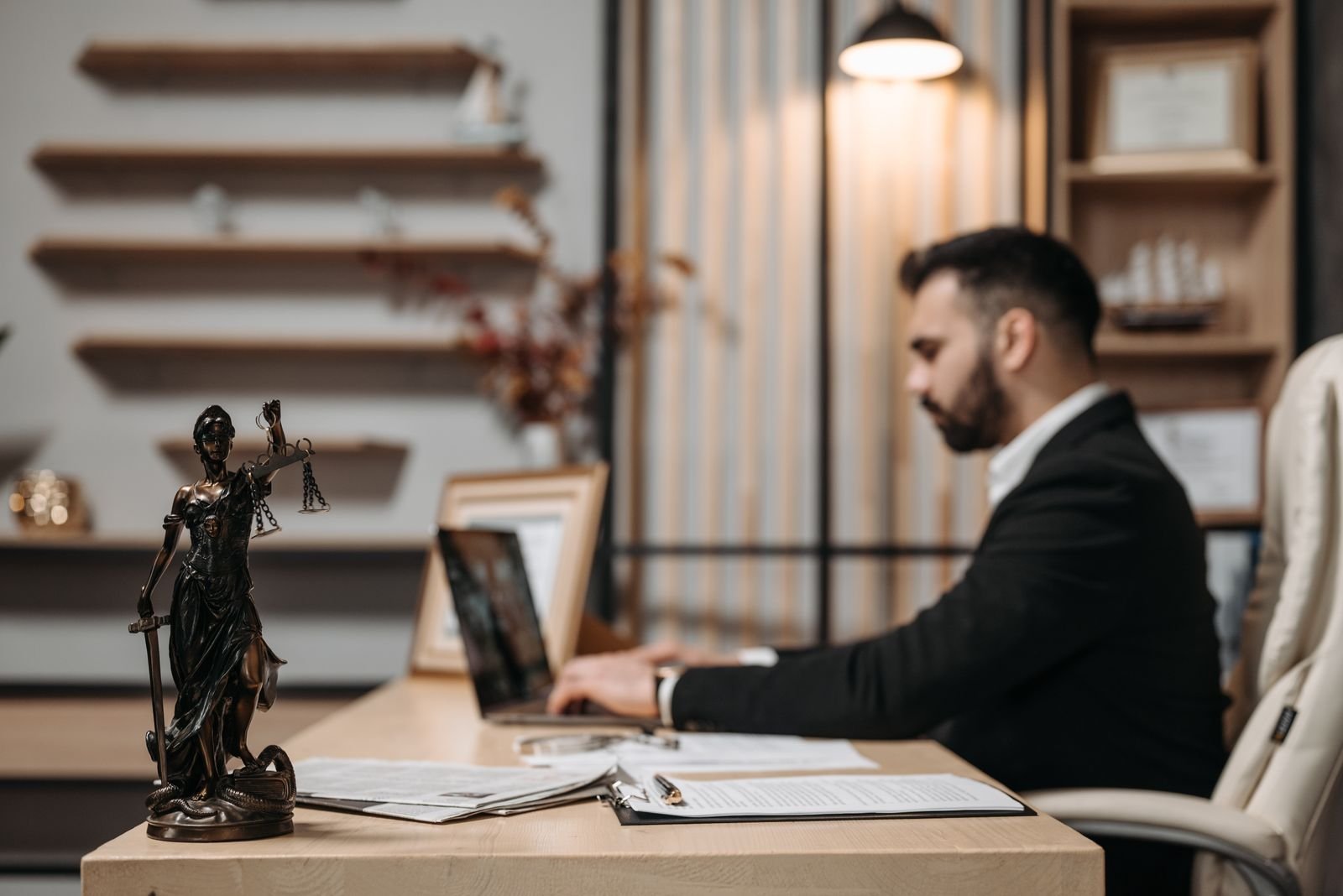 Lawyer working on a laptop beside a Lady Justice statue, illustrating legal AI tools like Harvey