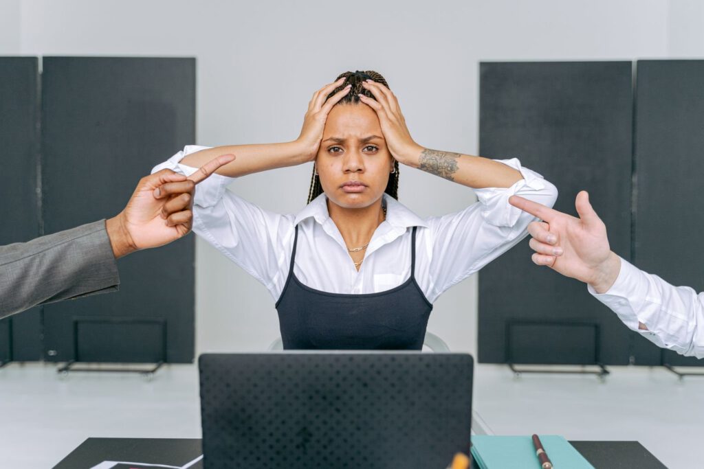 Distressed employee at a laptop with colleagues pointing at her, illustrating a hostile work environment