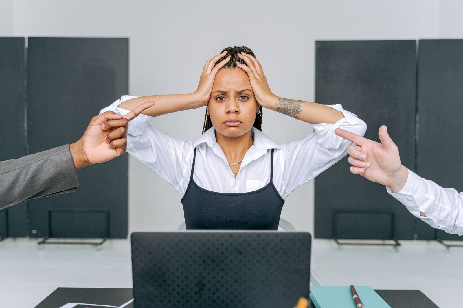 Distressed employee at a laptop with colleagues pointing at her, illustrating a hostile work environment