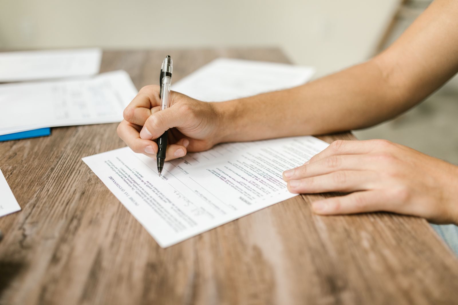 Close-up of a person filling out a printed form with a black pen at a wooden table