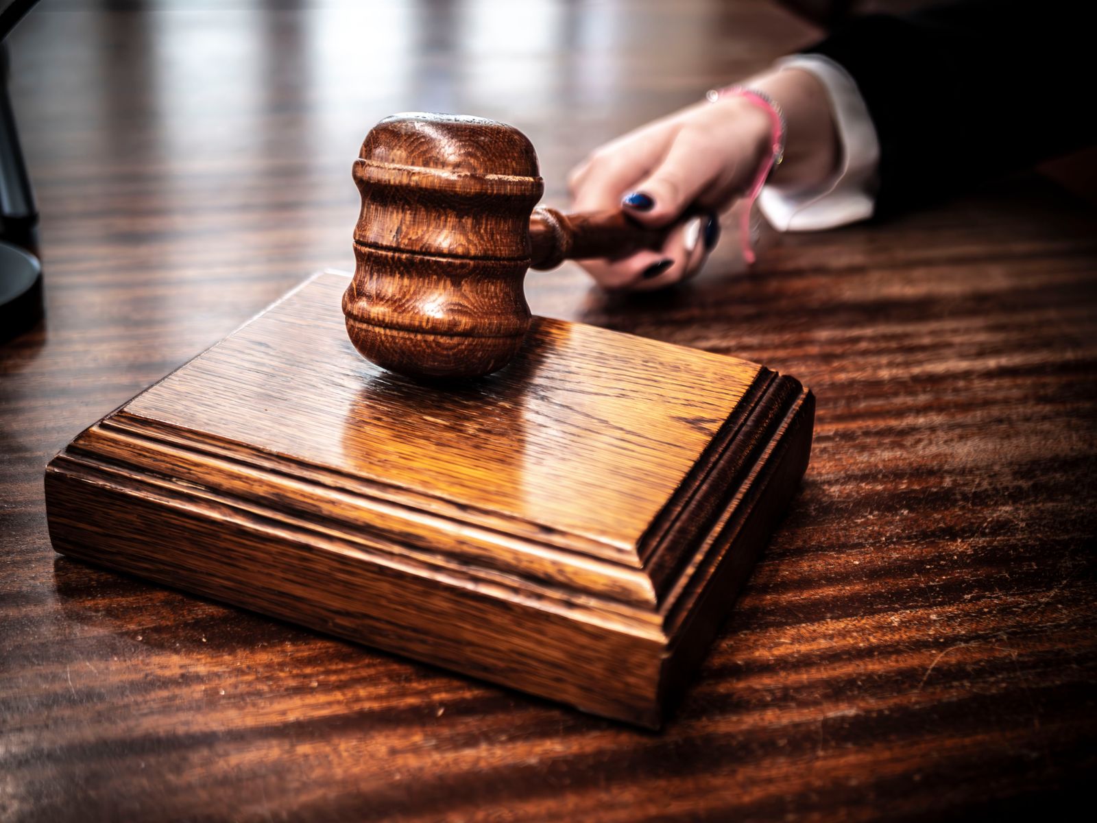 Hand holding a wooden gavel above its sound block on a polished dark wooden desk