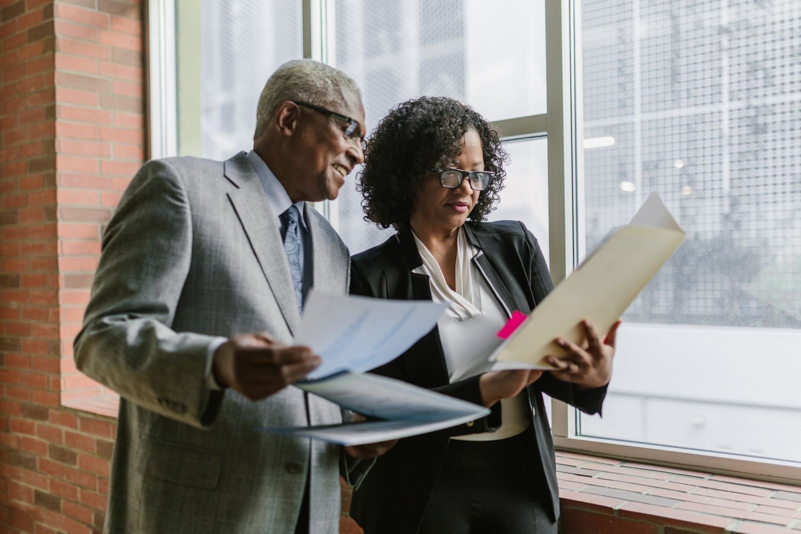Senior lawyer in a grey suit reviewing documents with a colleague beside a large office window