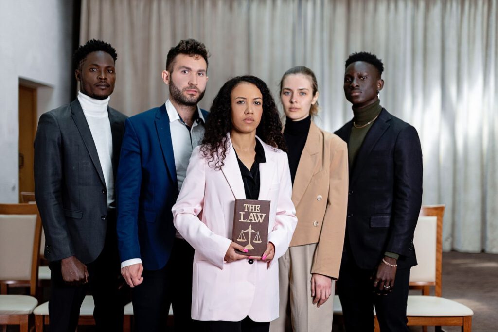 Five lawyers in business suits standing together in an office, the woman in front holding a book titled The Law