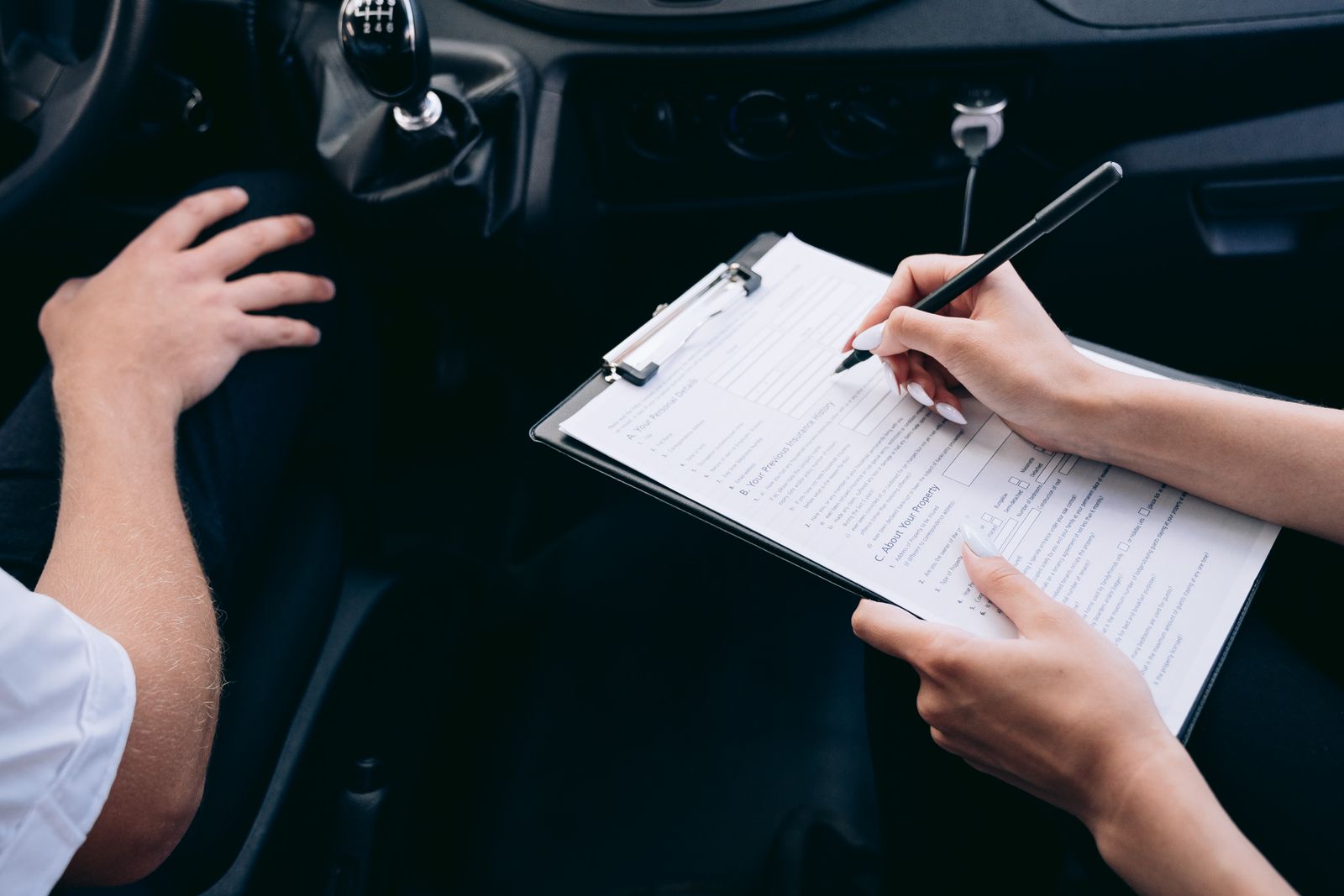 Person filling in an insurance claim form on a clipboard inside a car after an accident