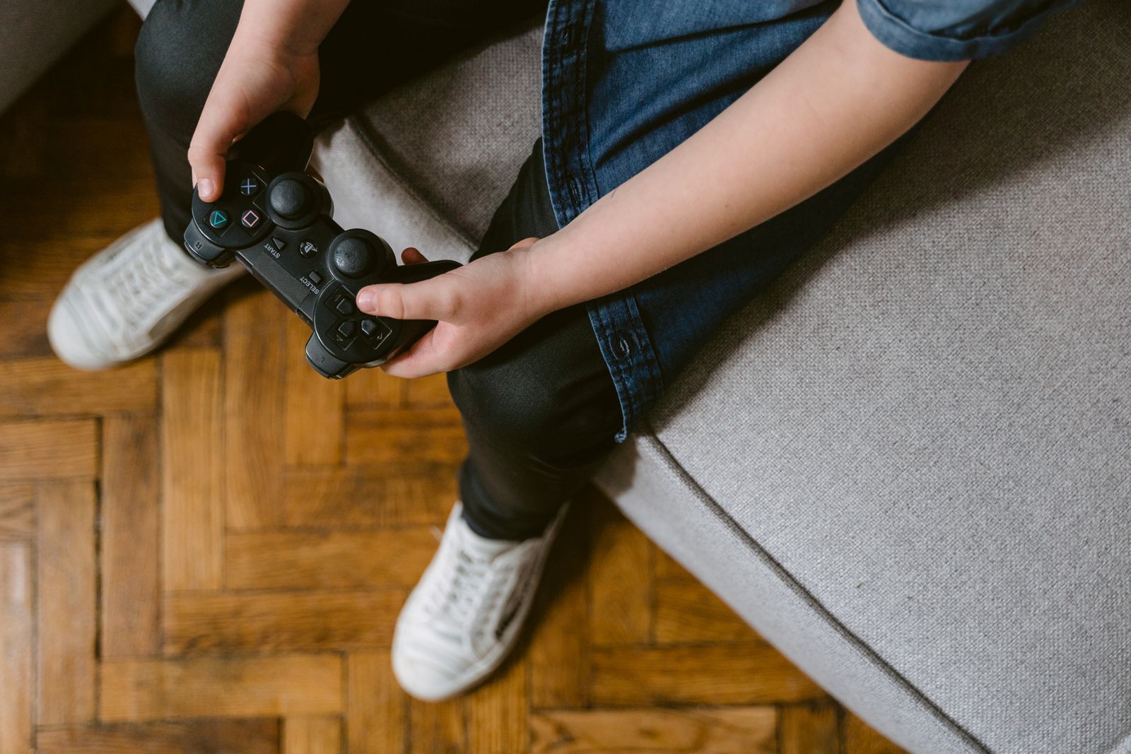 Child sitting on a sofa holding a game controller, seen from above with no face shown