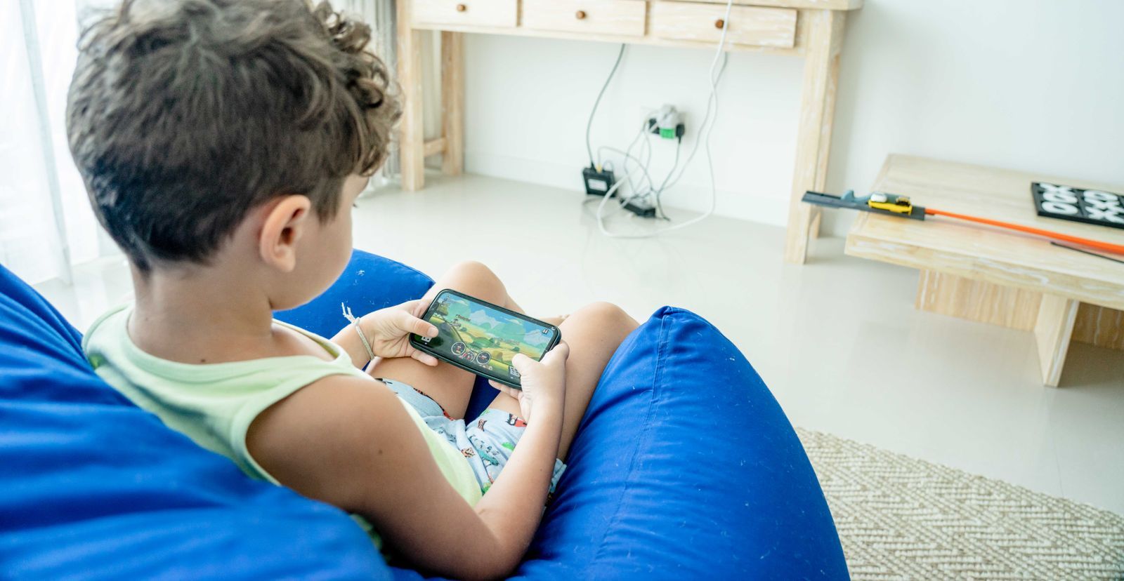 Child on a blue bean bag playing a game on a smartphone, seen from behind
