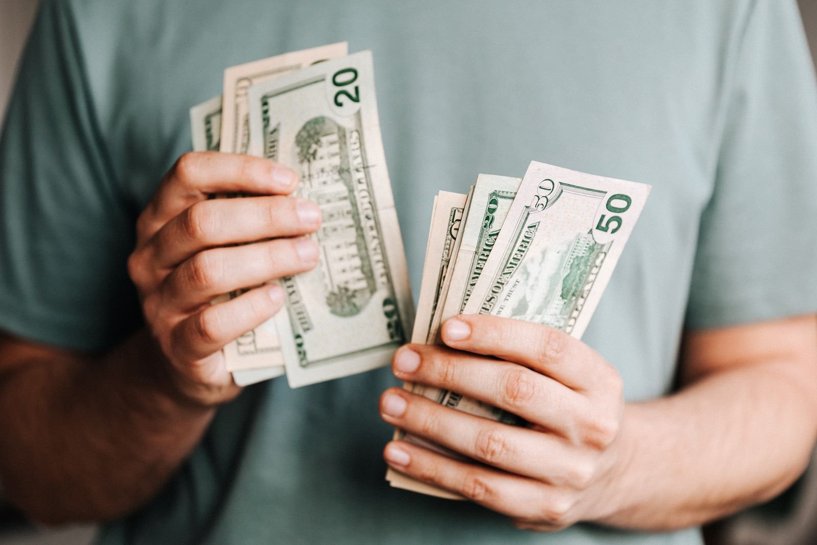 Person in a green T shirt counting a handful of twenty and fifty dollar banknotes