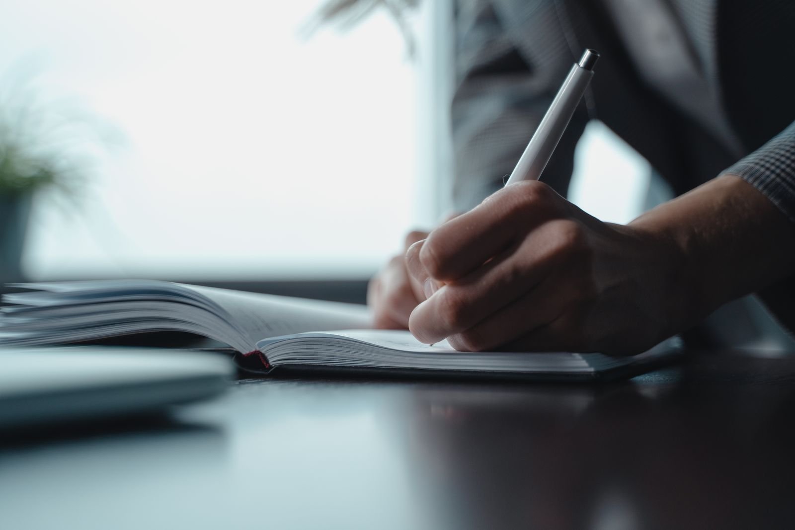 Close-up of a hand writing notes with a pen in an open notebook on a desk