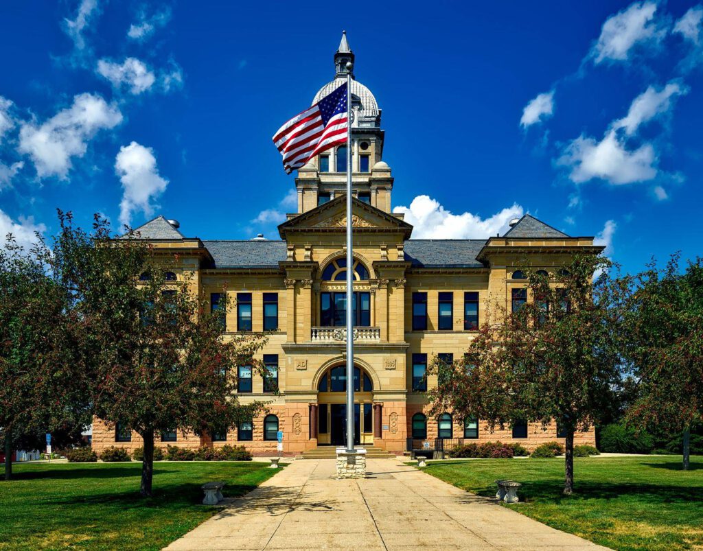 Historic stone county courthouse with a US flag flying on a pole in front under a bright blue sky