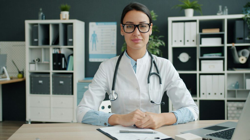 A female doctor wearing a stethoscope sits at her desk